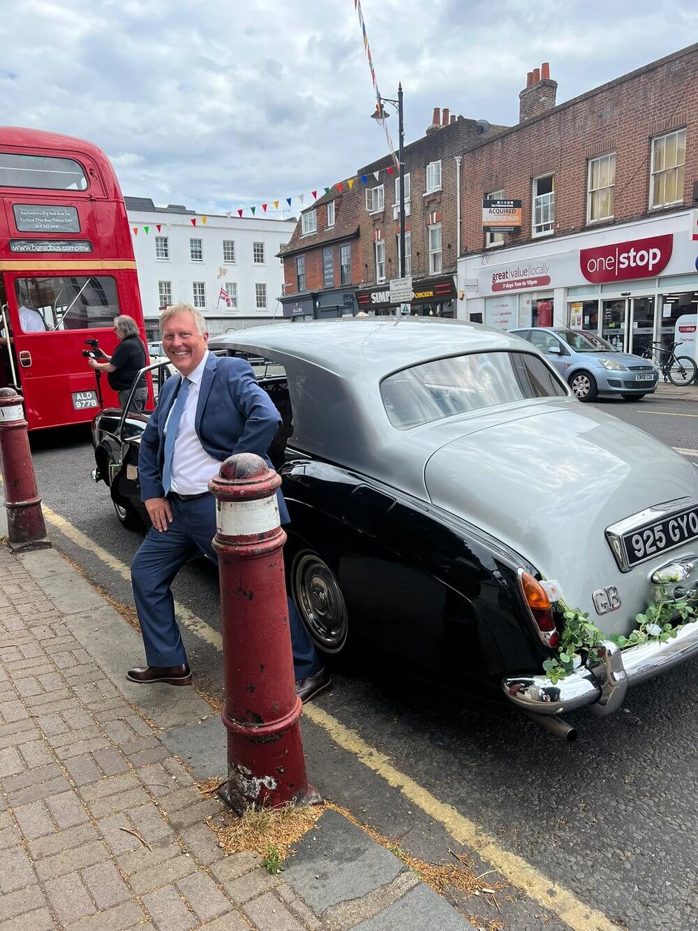 Man in suot smiling in front of luxury wedding car